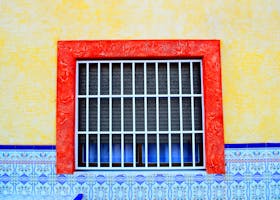 Colorful window with security bars surrounded by vibrant walls and intricate tiles.